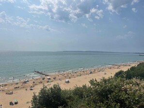 Ein Strand mit Zelten und Menschen, ein Steg, der sich ins Wasser erstreckt, und ein klarer Himmel.