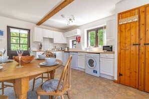 A modern kitchen with white cabinets, a wooden dining table, and a washing machine. - Rural Farm Cottage | Outside Space | 2bds & 2baths (Stelling Minnis)