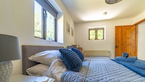 A bedroom with a bed, a nightstand, a lamp, a window, and a door.
