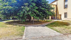 Un sentier bordé d’arbres mène à un bâtiment doté d’un toit en tuiles et d’une fenêtre grillagée.