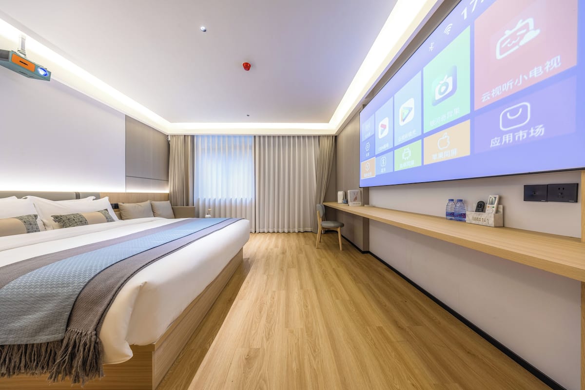 A modern hotel room with a large bed, a desk, and a wall-mounted TV displaying various apps.