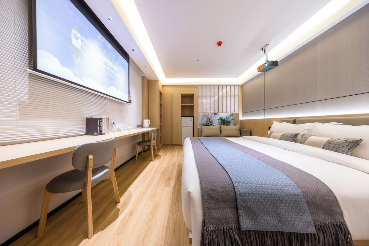 A modern hotel room with a large bed, a desk, and a projector screen.
