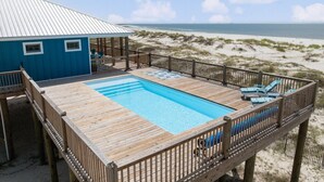 Ein Holzdeck mit Pool, einem blauen Gebäude und Blick auf den Strand.