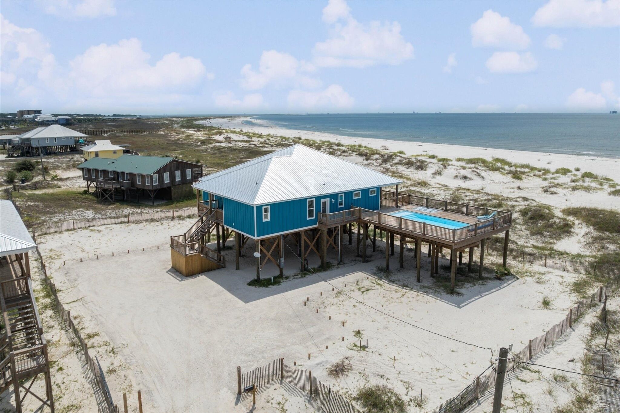 Een strandhuis met een groot blauw huis, een zwembad en een pier die in de oceaan uitsteekt.