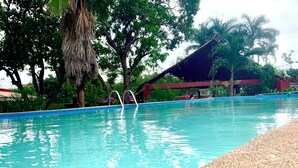 Una piscina de agua cristalina, rodeada de árboles y una zona cubierta.