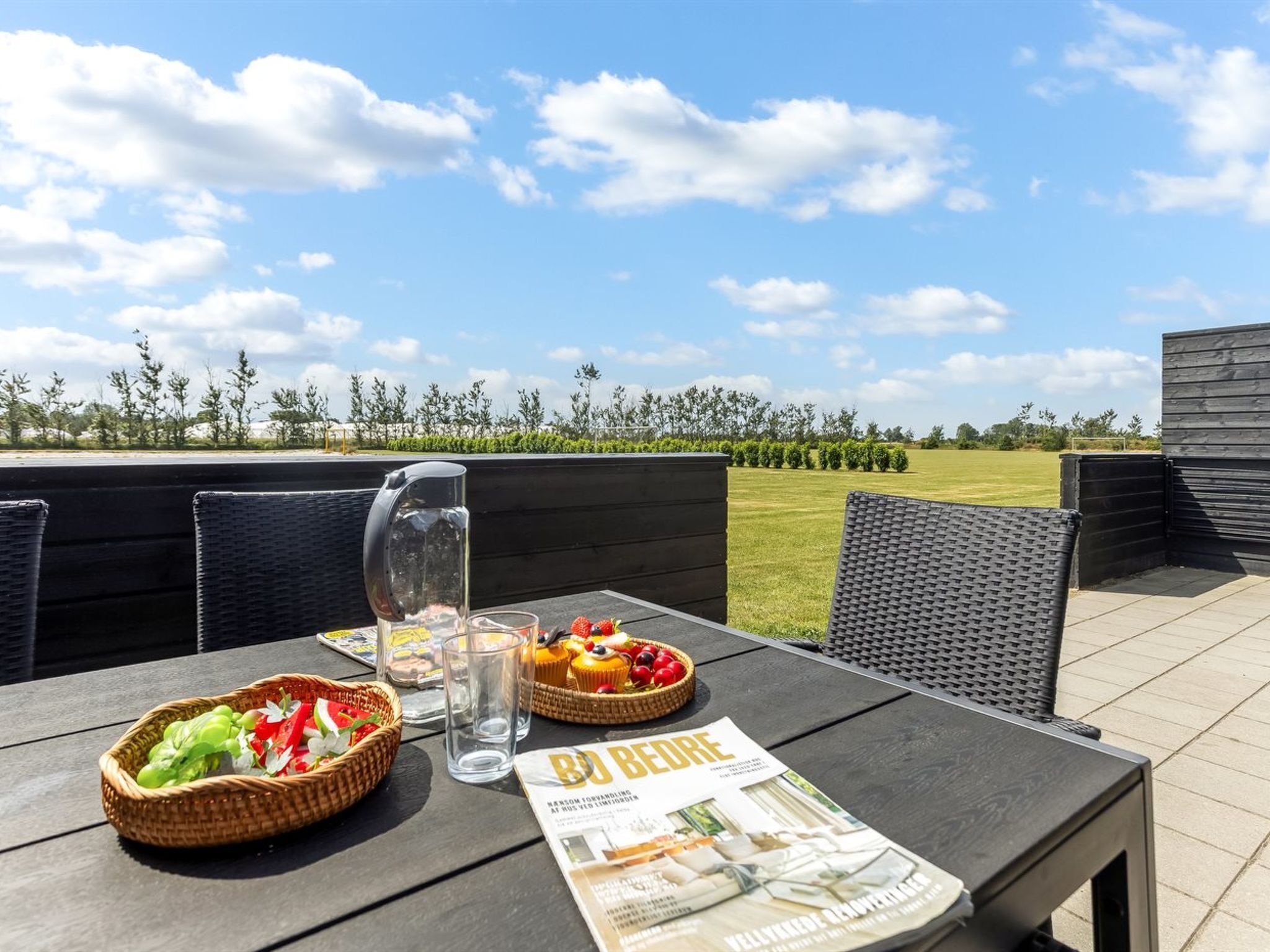 An outdoor dining area with a table set for two, a magazine, and a basket of vegetables.