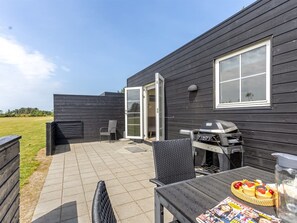 Een terras met een barbecue, buitenmeubels en een tafel met eten.