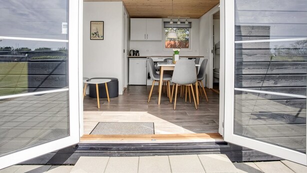 Une cuisine moderne avec des meubles blancs, un coin repas avec des chaises grises et un plafond en bois.
