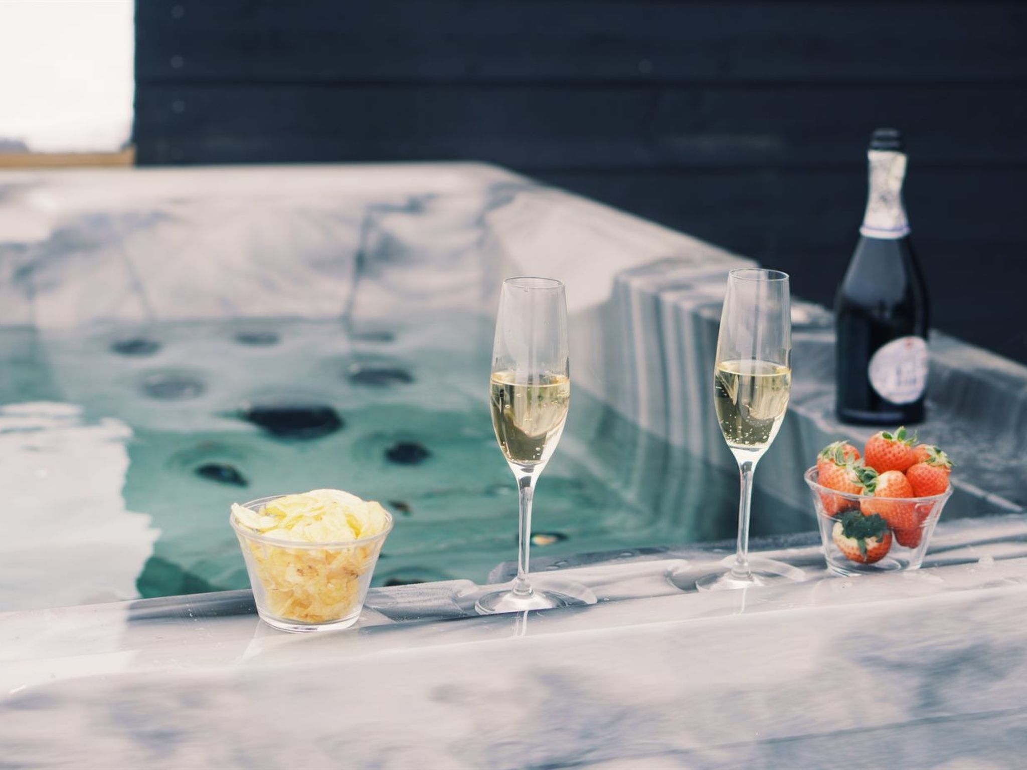 A hot tub with two glasses of white wine and a bowl of fruit.