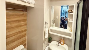 A bathroom with a toilet, sink, mirror, towel rack, and a shelf with towels.