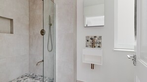 Ett modernt badrum med en duschavdelning med glasväggar, en vit tvättställ med en väggbeklädnad av marmor och en stor spegel ovanför tvättstället.