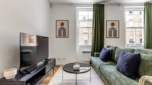 A modern living room with a flat-screen TV, green sofa, and two framed artworks. - Blueground | Fitzrovia, view, nr British Museum (London)
