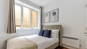 A bedroom with a bed, a window with curtains, a radiator, and two framed artworks on the wall. - Blueground | Fitzrovia, view, nr British Museum (London)
