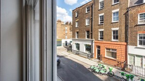 A view from a window overlooking a street with brick buildings, a parked bicycle, and a sign for a cafe. - Blueground | Fitzrovia, view, nr British Museum (London)