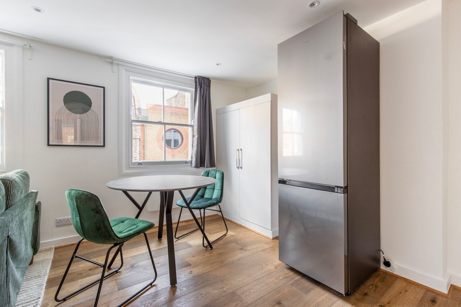 A modern kitchen with a built-in refrigerator, a dining table with chairs, and a window with curtains.