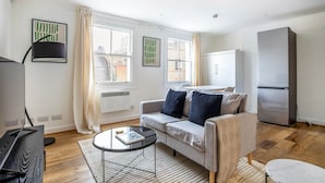 Un salon moderne avec un canapé gris, une table basse en verre, un lampadaire noir, un radiateur blanc et une armoire blanche.