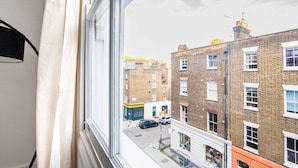 Une vue depuis une fenêtre donnant sur une rue bordée d’immeubles en briques, avec une voiture garée sur le côté et un ciel dégagé.