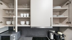A modern kitchen with a built-in microwave, stove, and toaster. It features white cabinetry and shelves for dishes and glasses.