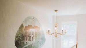 Eine Treppe mit Holzgeländer und weißer Brüstung, die zu einem Raum mit einem großen Fenster und einer Chandeliebre führt.