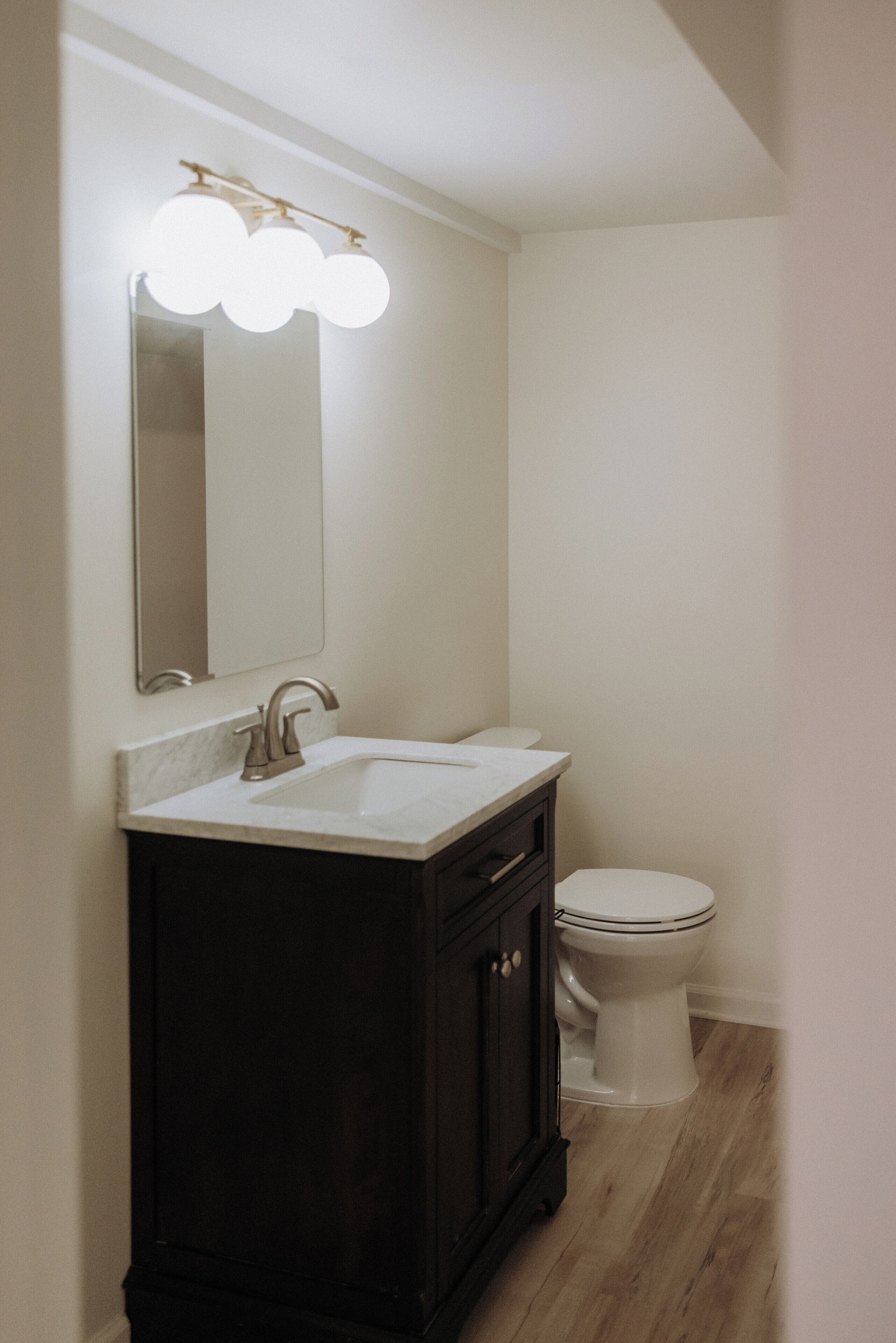 A bathroom with a white sink, dark wooden vanity, a mirror, and a toilet.