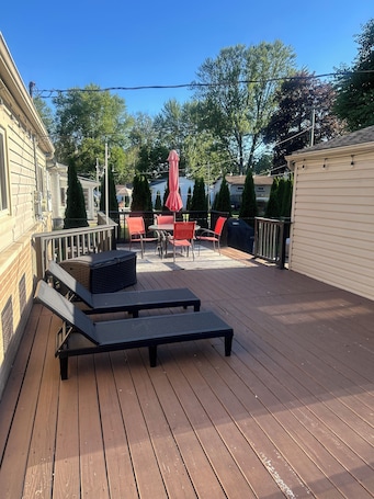 A wooden deck with lounge chairs and a table, surrounded by a railing and trees.