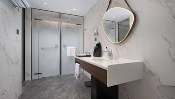 A modern bathroom with a marble floor, a large mirror with a gold frame, a white sink, and a glass shower enclosure.