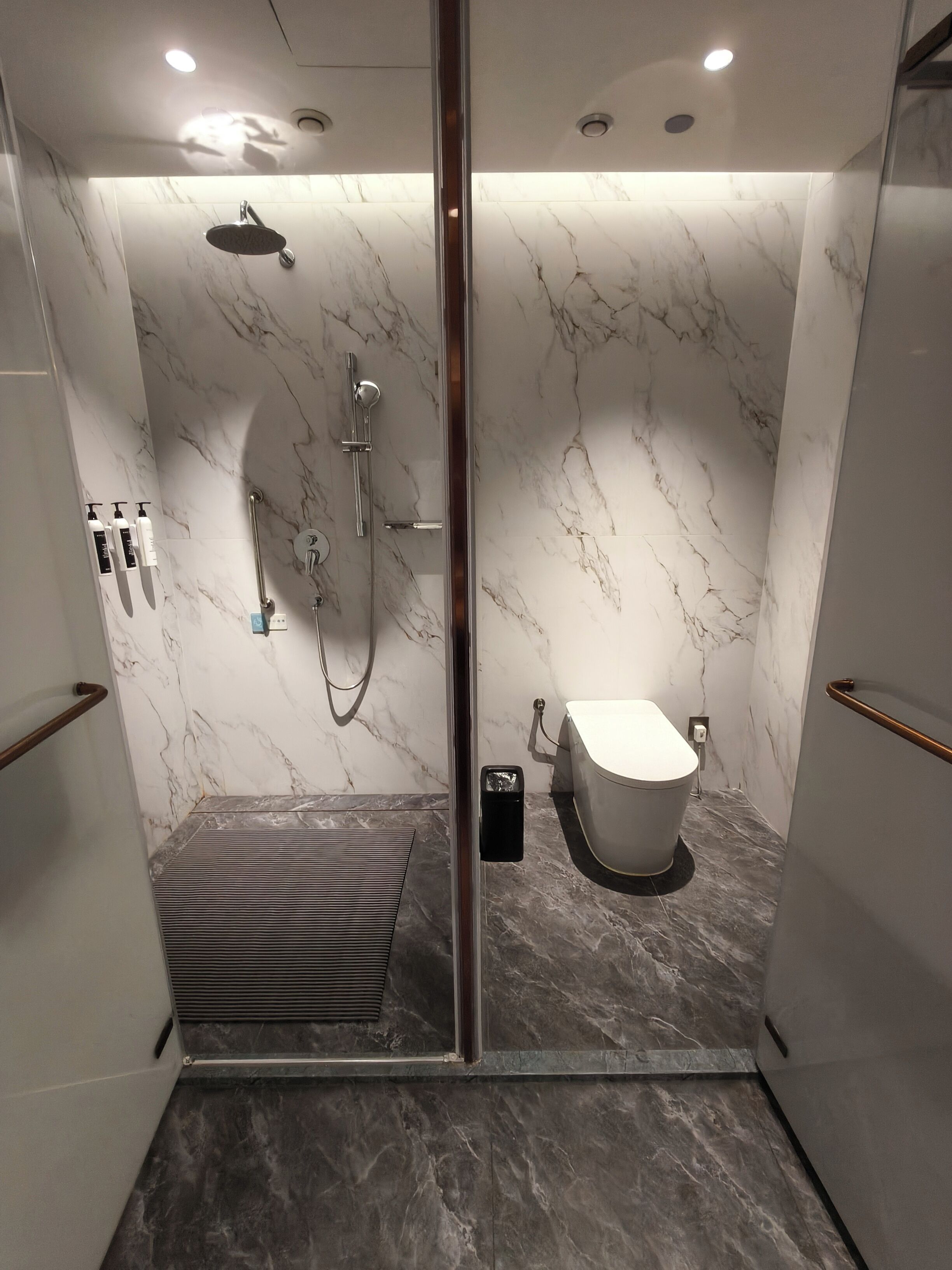 A modern bathroom with a glass-enclosed shower, a toilet, and a bench.