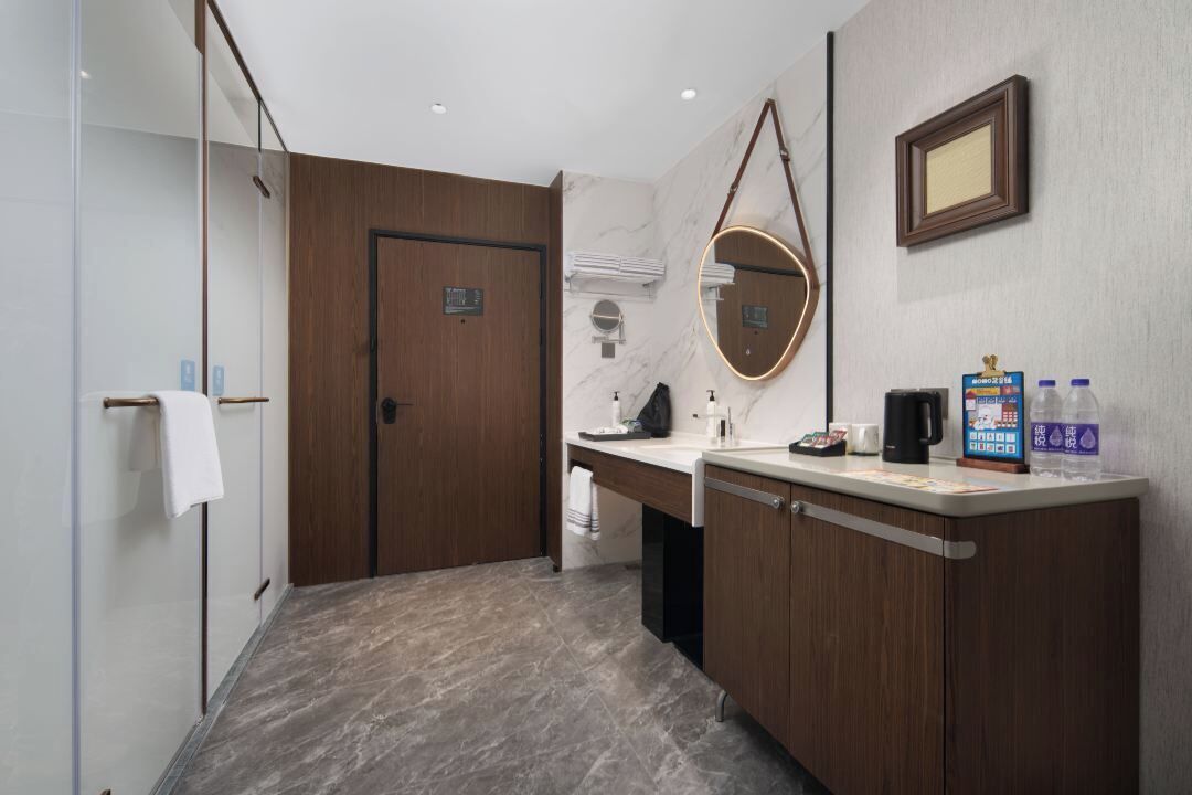 A modern bathroom with a wooden door, a marble wall, a round mirror, and a counter with toiletries.