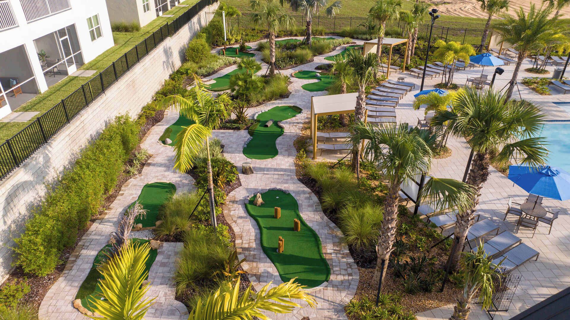 Un campo de golf con zona de piscina, palmeras y sillones de descanso.
