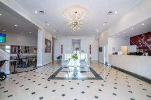 A hotel lobby with a reception desk, seating area, and a large chandelier.
