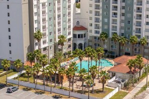 A multi-story hotel with a central courtyard featuring a swimming pool, palm trees, and outdoor seating.
