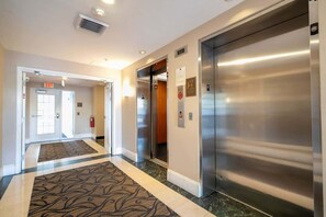 Un hall d’hôtel doté d’un sol recouvert de moquette, d’un ascenseur et d’une porte indiquant « SORTIE ».