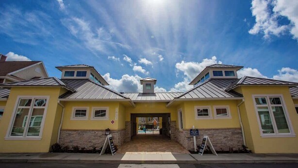 A yellow building with a central entrance, two side wings, and a metal roof.