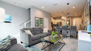 A modern living room with a sofa, coffee table, and a staircase leading to a kitchen area.