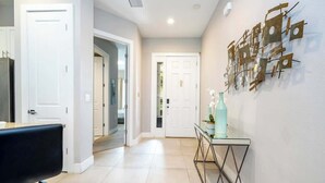 A hallway with a white door, a glass console table with decorative items, and a wall art piece.