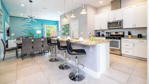 A modern kitchen with white cabinets, a central island with bar stools, and stainless steel appliances.