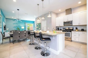 A modern kitchen with white cabinets, a central island with bar stools, and stainless steel appliances.