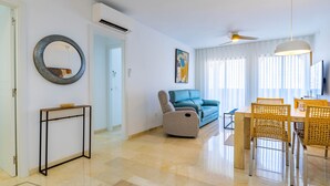 A modern living room with a sofa, a dining table with chairs, a round mirror, and a ceiling fan. - Inftour Medici 6L Apartamento (Calp)