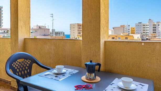 A balcony with a table set for two, a coffee maker, and a pair of glasses. - Inftour Medici 6L Apartamento (Calp)