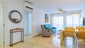 Un salon moderne avec un canapé, une table à manger et des chaises, un miroir rond et un ventilateur de plafond.