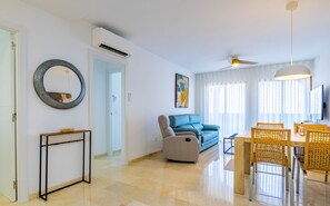 A modern living room with a sofa, a dining table with chairs, a round mirror, and a ceiling fan.
