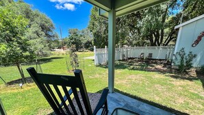 A covered patio with a rocking chair and a small table, overlooking a well-maintained lawn and white fence. - Contemporary 2 bedroom house in San Marcos close to campus, downtown & the river (San Marcos)