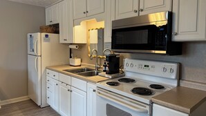 A modern kitchen with white cabinetry, a stainless steel refrigerator, a microwave, a stove, and a sink.