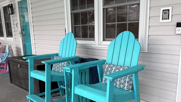A porch with two turquoise Adirondack chairs, a matching table, and a gray patterned rug.