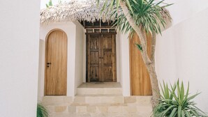 A courtyard with a wooden door, a thatched roof, and palm trees. - 3Br Khana in Canggu With 3 Bedrooms and 3 5 Bathrooms (Canggu)