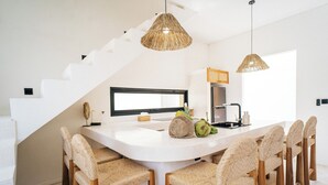 A modern kitchen with a white island, wicker chairs, and a staircase. - 3Br Khana in Canggu With 3 Bedrooms and 3 5 Bathrooms (Canggu)