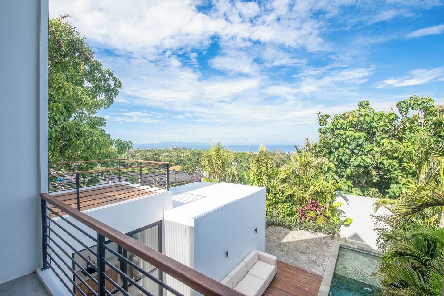 A modern rooftop with a pool, surrounded by lush greenery and a clear sky.