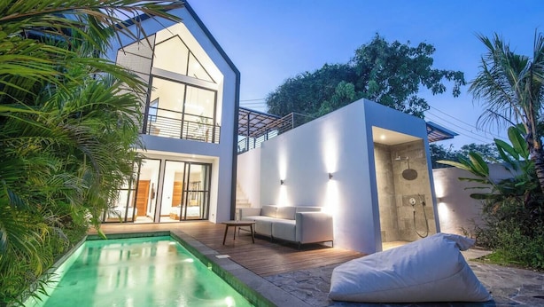Una casa moderna de dos pisos con piscina, zona de estar exterior y un área de ducha separada.