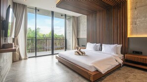 A modern bedroom with a large bed, a wooden headboard, and a view of greenery through large windows.