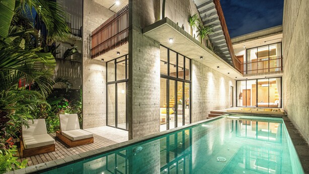 A modern indoor swimming pool with lounge chairs, concrete walls, and a wooden deck.